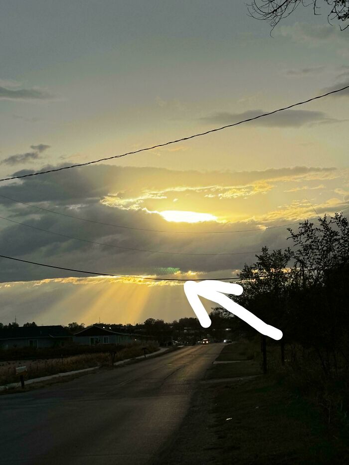 Sunset over empty road with sunbeams through clouds and a green lens flare, suggesting glitches in the matrix
