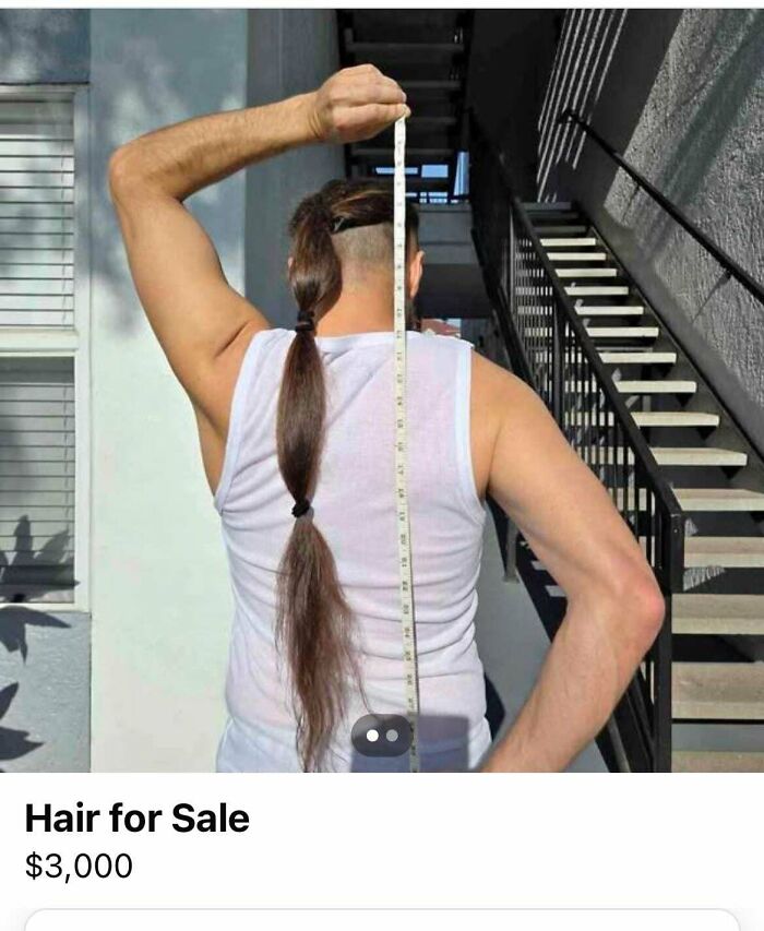 Man measuring long braided hair to sell online, back view wearing white tank top by stairs.