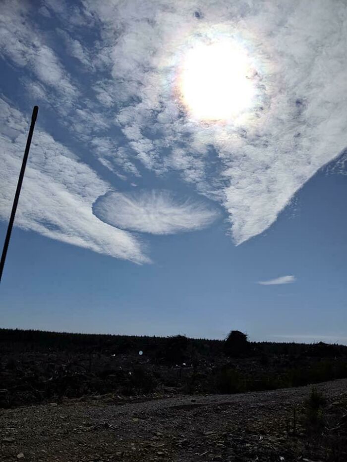 Circular hole in cloud near bright sun over barren field, reminiscent of glitches in the matrix
