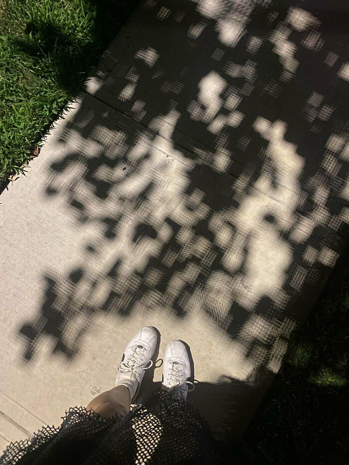 White sneakers on sidewalk with pixelated leafy shadows resembling glitches in the matrix