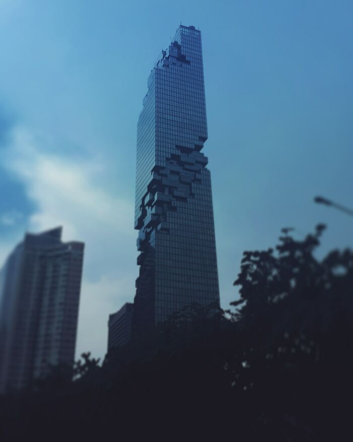 Glass skyscraper with blocky pixel-like protrusions against blue sky, evoking glitches in the matrix