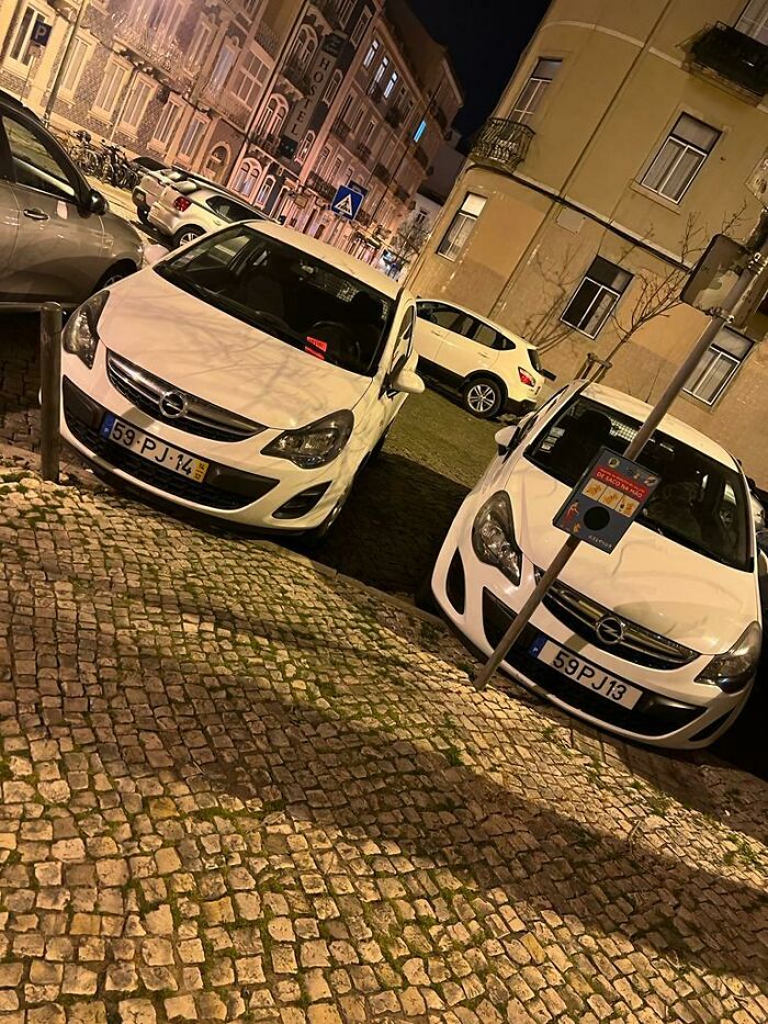 Two identical white cars on cobblestone street at night, evoking glitches in the matrix with duplicate license plates