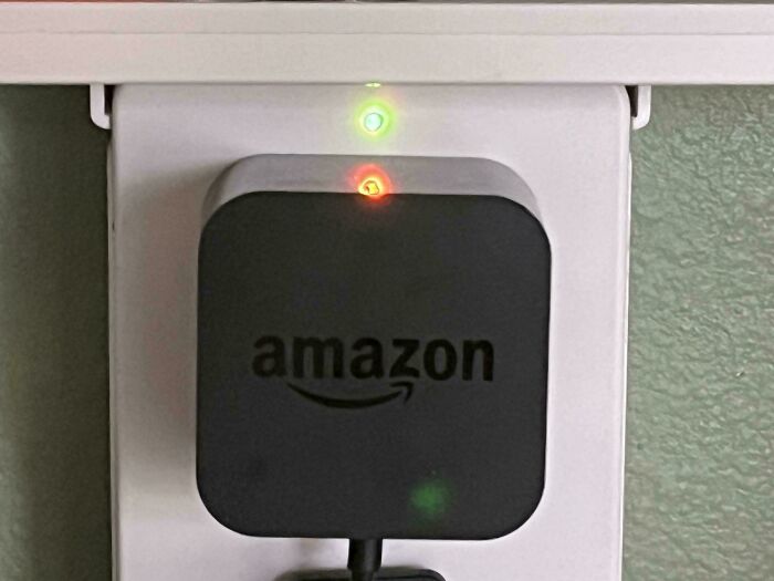 Amazon plug adapter in wall outlet with red and green indicator lights, evoking glitches in the matrix