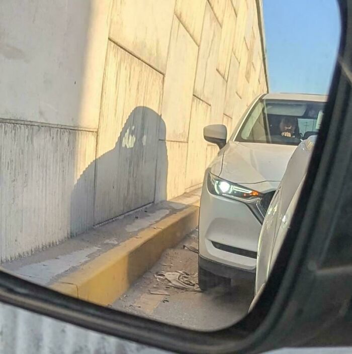 White car in a narrow lane with a wall shadow that looks like a hooded figure, glitches in the matrix