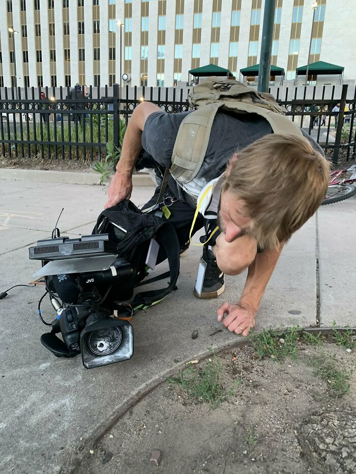 Man kneeling on sidewalk inspecting broken video camera gear after he woke up expecting a normal day