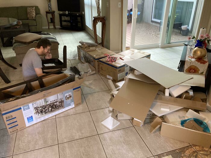 Man surrounded by cardboard boxes and packing debris assembling furniture after woke up expecting a normal day