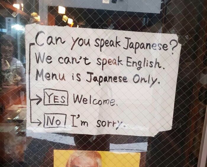Handwritten sign showing a humorous Japan English translation error about language and menu availability in a restaurant window.