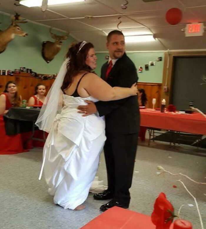 Bride in a wedding dress revealing questionable taste dancing with groom at a casual indoor reception with guests in background