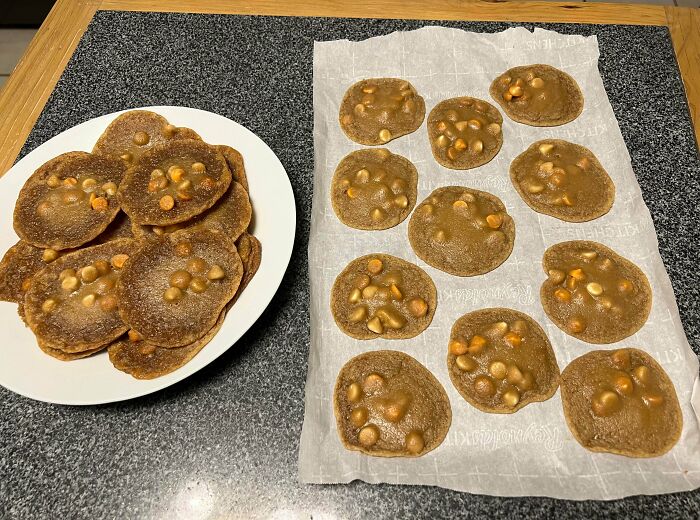 Burnt and misshapen cookies with caramel chips on parchment paper and a plate, showing dessert ruining fails.