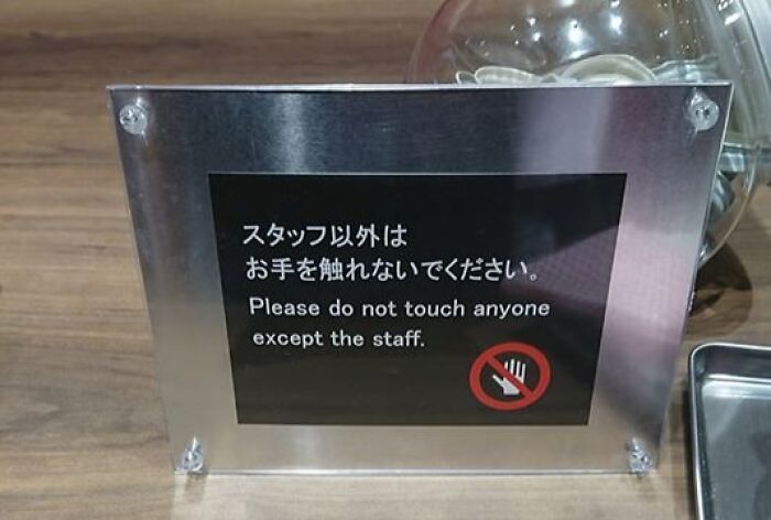 Japanese translation fail sign in a metal frame humorously warning not to touch anyone except staff.