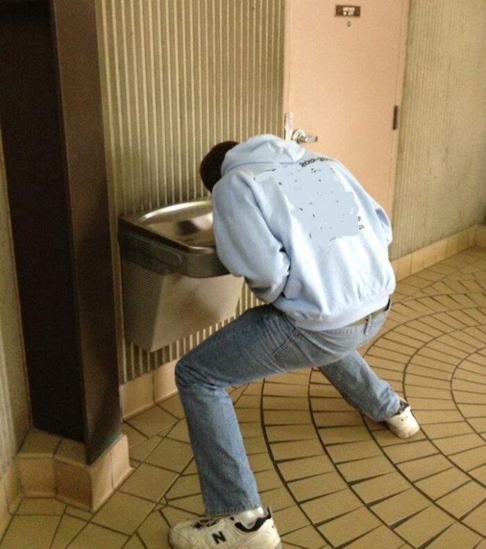 A tall person bending awkwardly to drink from a low water fountain, highlighting struggles only tall people face.
