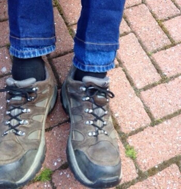 Close-up of worn hiking shoes and rolled-up jeans on a brick pavement illustrating common tall people struggles.