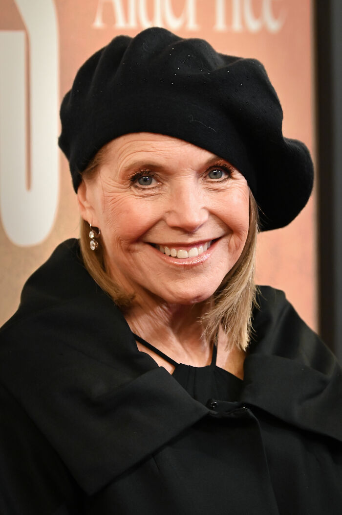 Smiling female broadcaster in black beret and coat at an event, close-up portrait.