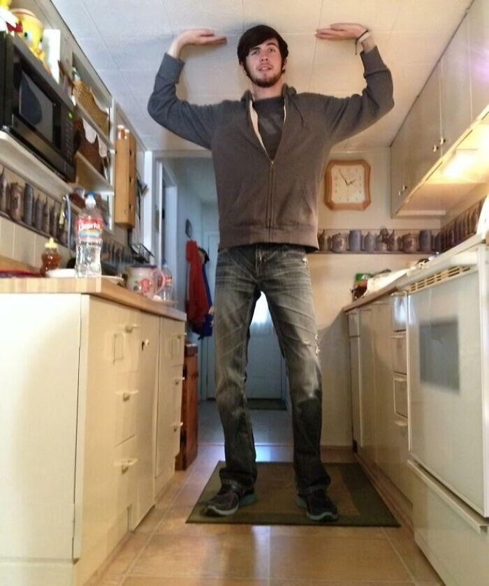 Tall person in a kitchen measuring their height against a low ceiling, illustrating struggles only tall people face indoors.