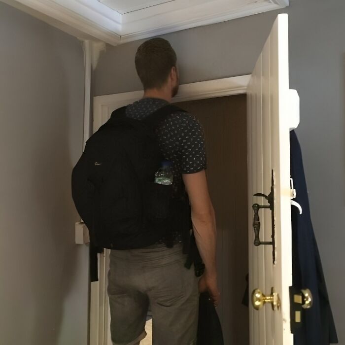 Tall person struggling to fit through a low doorway, highlighting common struggles only tall people face.