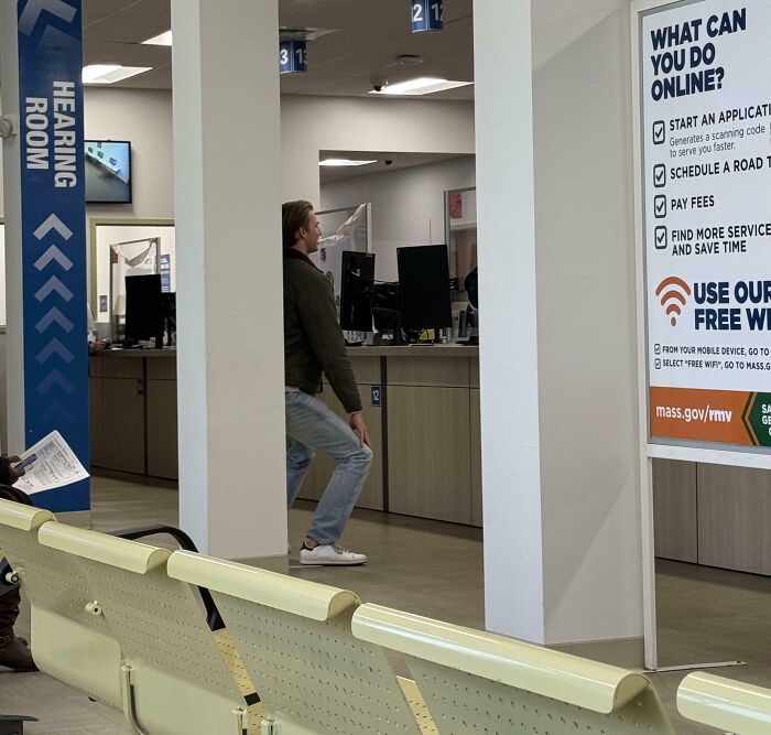 Tall person ducking to avoid hitting head on a low ceiling beam inside a public office waiting area.