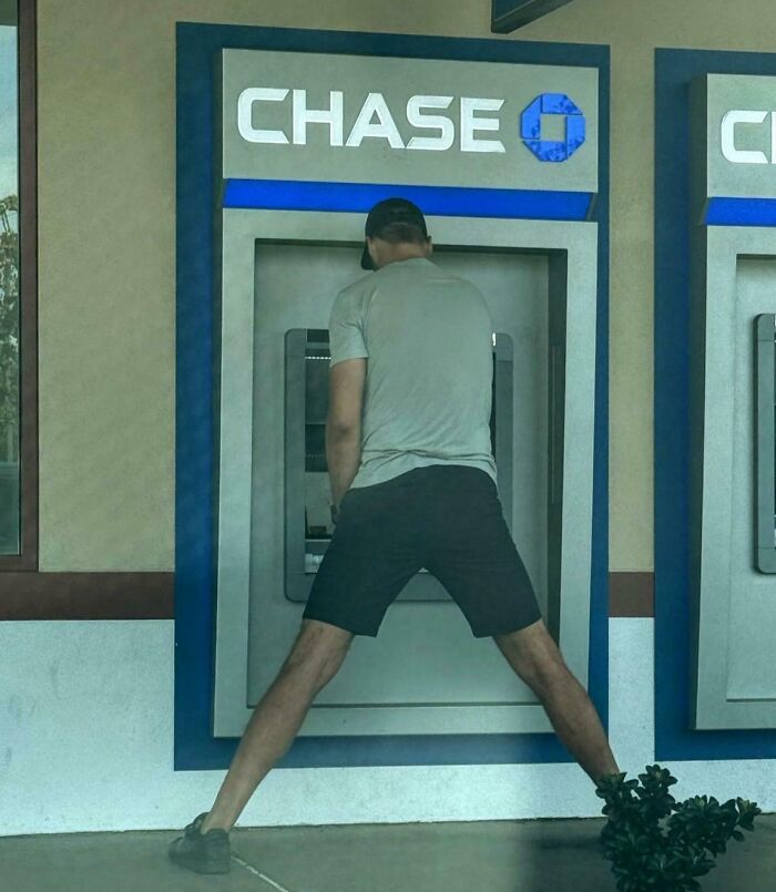 Tall man struggling to use an ATM machine due to height challenges faced by tall people in everyday situations.