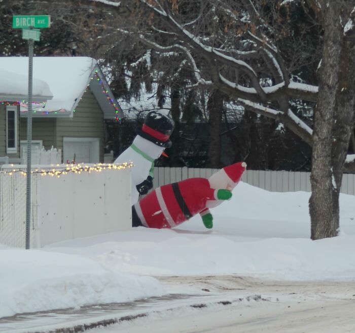 Inflatable snowman and Santa decorations toppled over in snow, creating a confusing and funny winter scene.