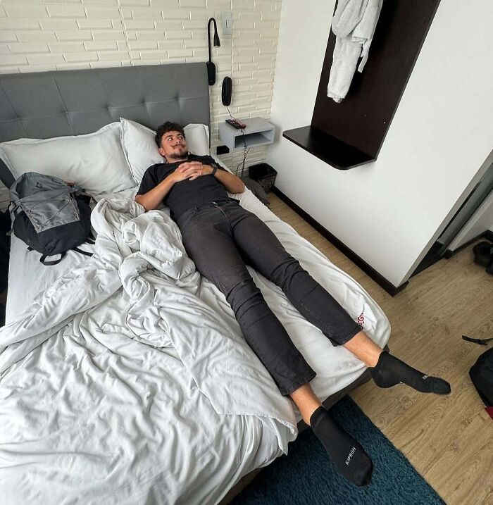 Tall man lying on a small bed illustrating common struggles only tall people face in daily life.