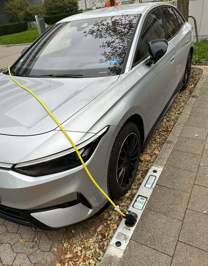 Silver electric car charging at a curbside station, showcasing impressive sustainable technology countries implemented.