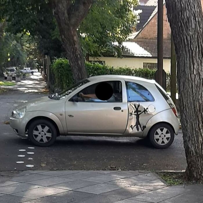 Silver car parked on the street with a playful black silhouette decal and painted paw prints on the ground nearby.
