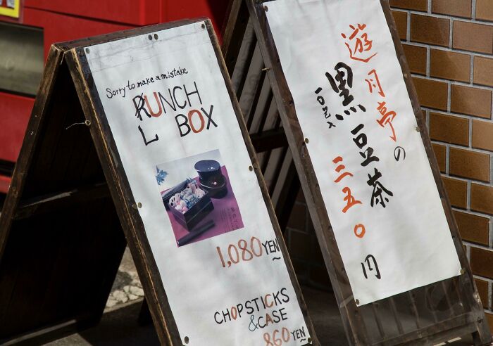 Wooden signs showing funny Japan English translation errors with lunch box and chopsticks prices displayed on a street corner.