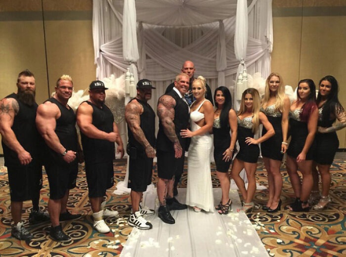 Bride and groom posing with muscular groomsmen and women in black dresses in an awkward wedding photo moment.