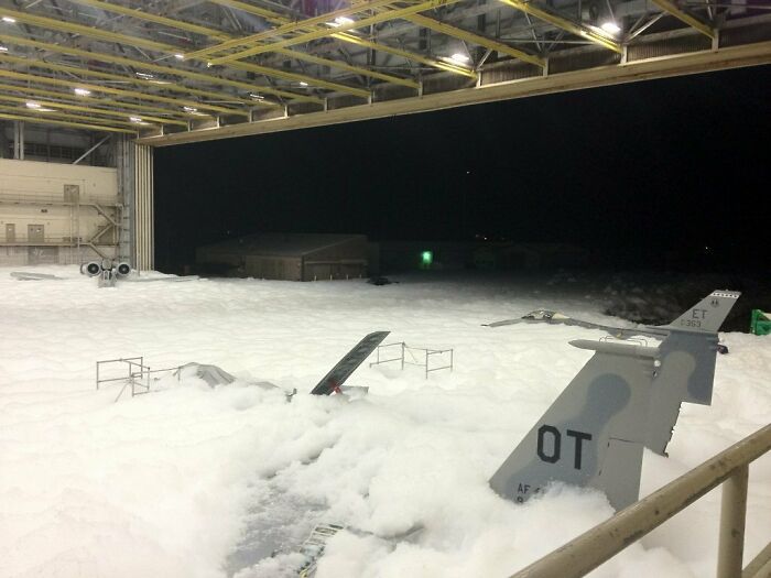Military aircraft covered in foam inside hangar showing unfortunate and expensive fails in maintenance or safety procedures.