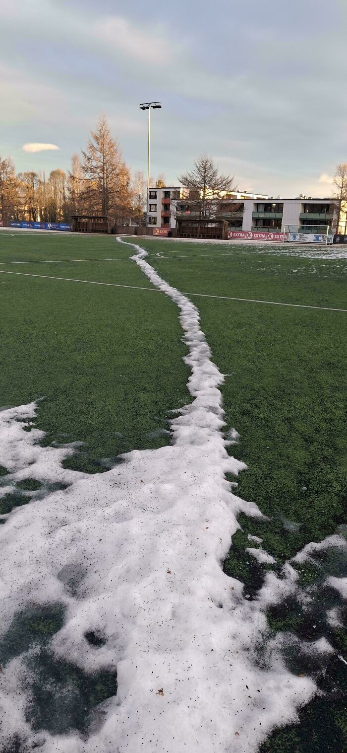 Snow forming a desire path on a green sports field, illustrating how people walk differently than city plans predict.