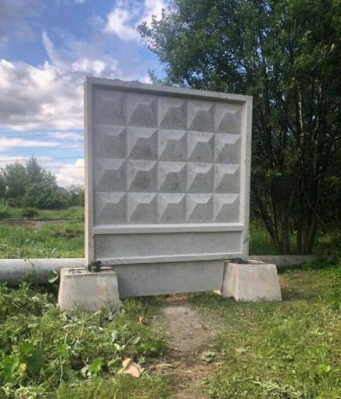 Concrete city barrier blocking a paved path with a visible desire path worn through the grass underneath.
