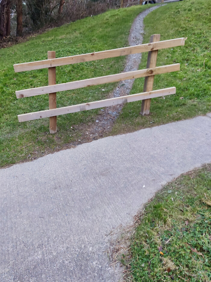 A desire path worn through grass behind a wooden fence, showing how people walk differently than planned city paths.