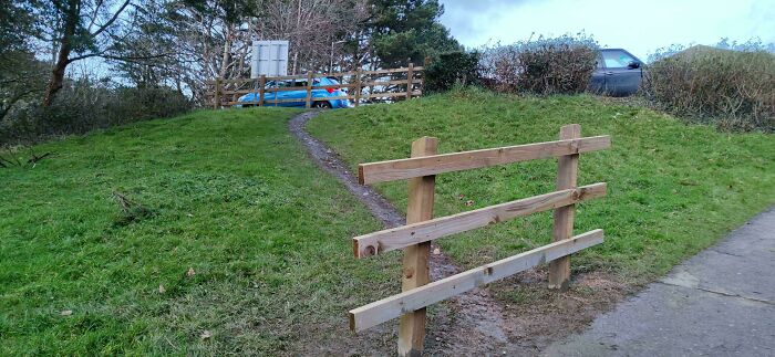 A desire path worn through grass beside a wooden fence, showing how people walk differently from city planning.