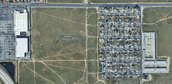 Aerial view of desire paths cutting across open land beside a residential neighborhood, illustrating city planning vs real walking routes.