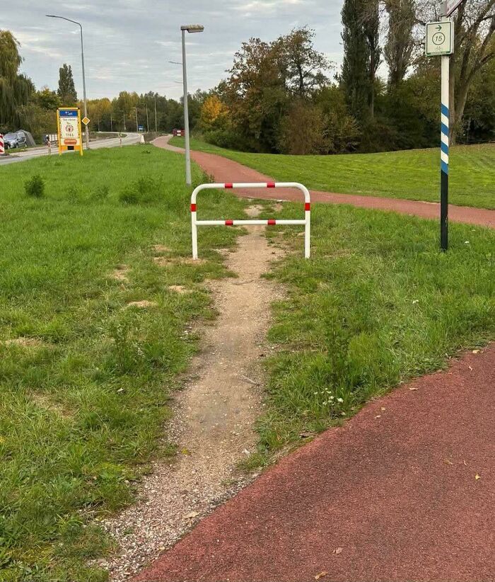 A desire path cuts through grass, showing how people walk instead of following the city’s planned walkway.