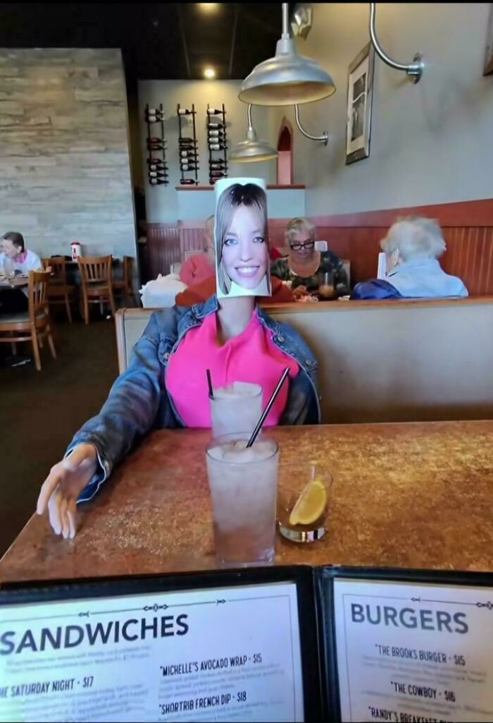 Person sitting in a restaurant booth with a humorous photo mask face, one of confusing pictures that are funny.