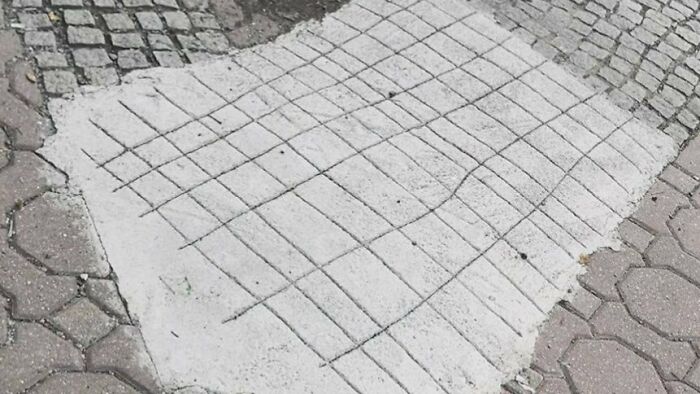 Patch of concrete with uneven grid lines on outdoor pavement, illustrating humorous Eastern European experience with quirky repairs.
