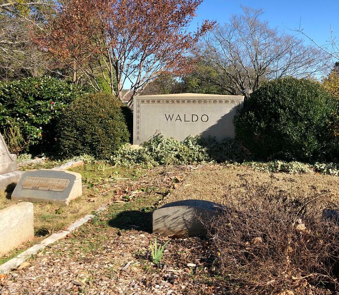 Gravestone marked Waldo in a quiet cemetery surrounded by bushes and autumn foliage in a confusing funny scene.