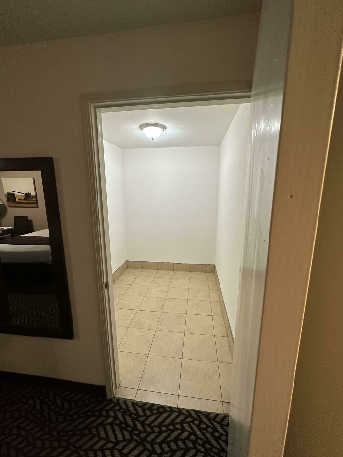 Small empty room with tiled floor and white walls in a dimly lit space, creating an unhinged and unexpected vibe.