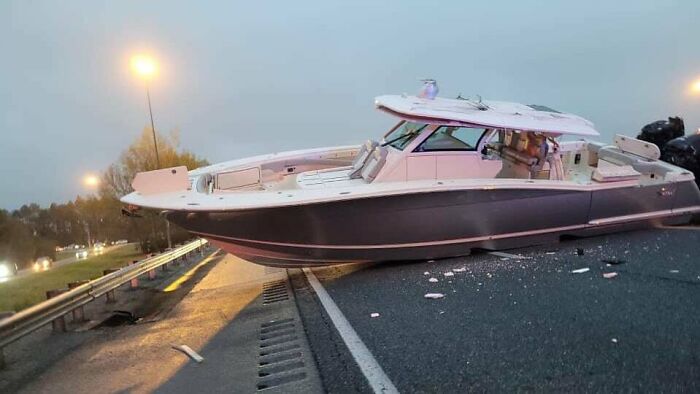 Boat stranded on a highway after an expensive and unfortunate fail, debris scattered on the road at dusk.