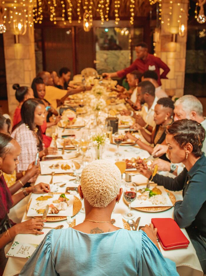 Large family dinner gathering with people sharing food and conversations, highlighting family secrets and connections.