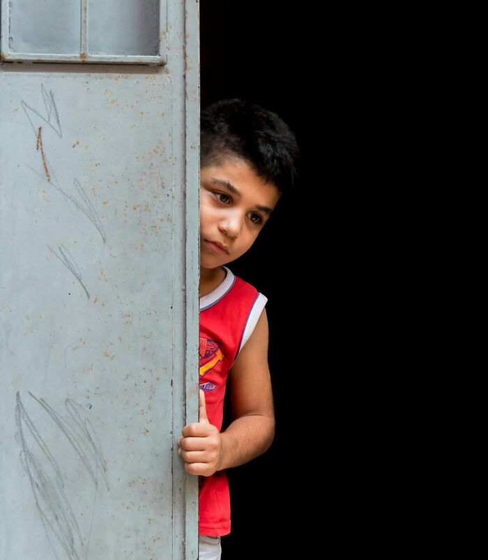 Young boy peeking from behind a door, symbolizing curiosity and mystery about family secrets and hidden stories.