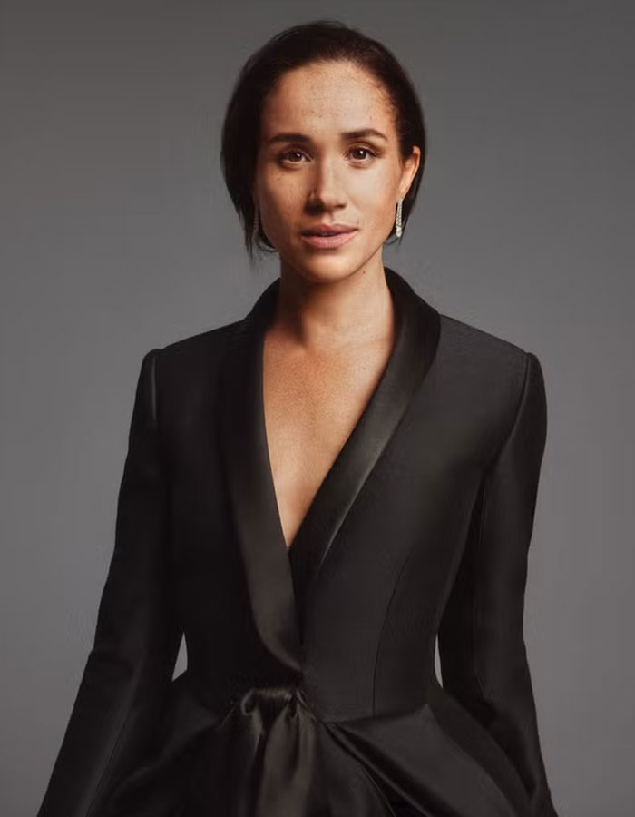 Meghan Markle in a stylish black outfit, posing against a gray background in a formal portrait session.
