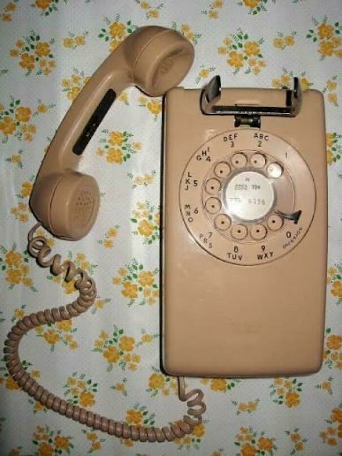Beige rotary dial phone with coiled cord on floral wallpaper, a nostalgic post to make you feel old as heck.