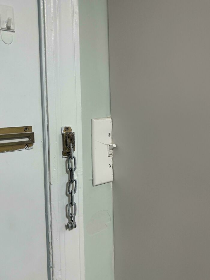 Light switch placed behind a door chain lock illustrating designers making dumb decisions creating problems.