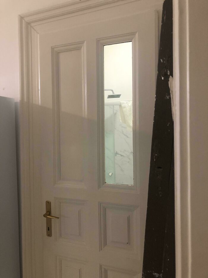 Door with a glass panel showing a shower inside, a design fail causing privacy problems nobody asked for.