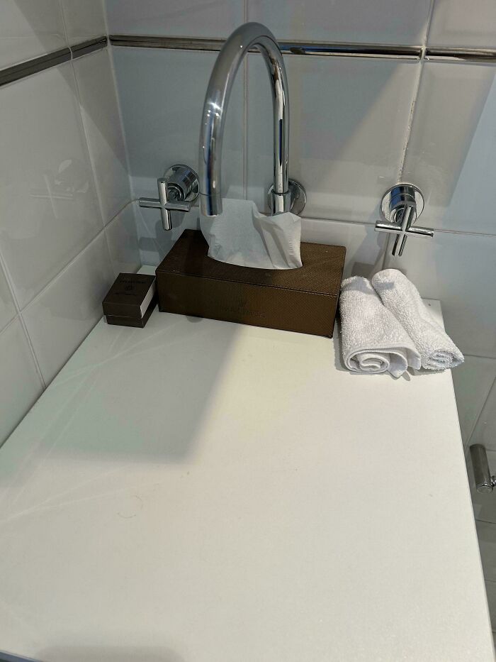 Bathroom faucet with tissue box placed under the spout, demonstrating dumb design decisions creating problems nobody asked for.