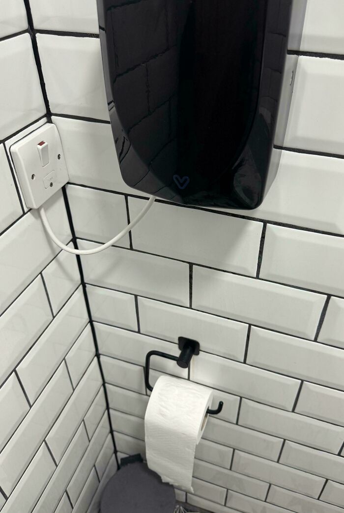 Toilet paper holder installed behind the toilet, illustrating dumb design decisions creating problems nobody asked for.