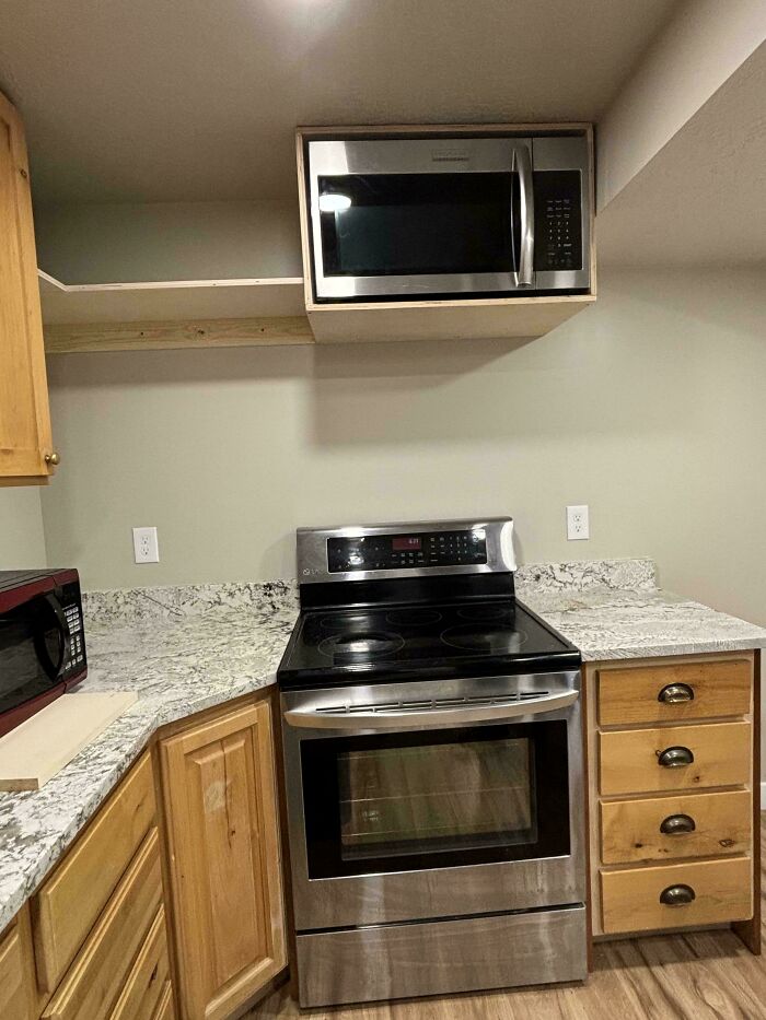 Microwave awkwardly placed above stove in kitchen showing designers made dumb decisions creating problems.