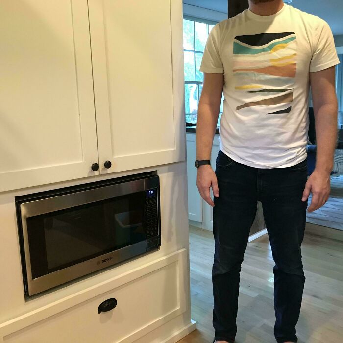 Man standing next to a poorly placed microwave embedded too low in kitchen cabinetry, showing a design problem.