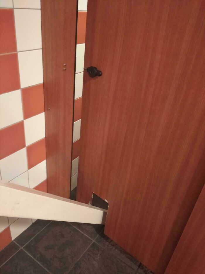 Bathroom stall door with a wooden plank awkwardly cut and inserted, showcasing dumb design decisions creating problems.